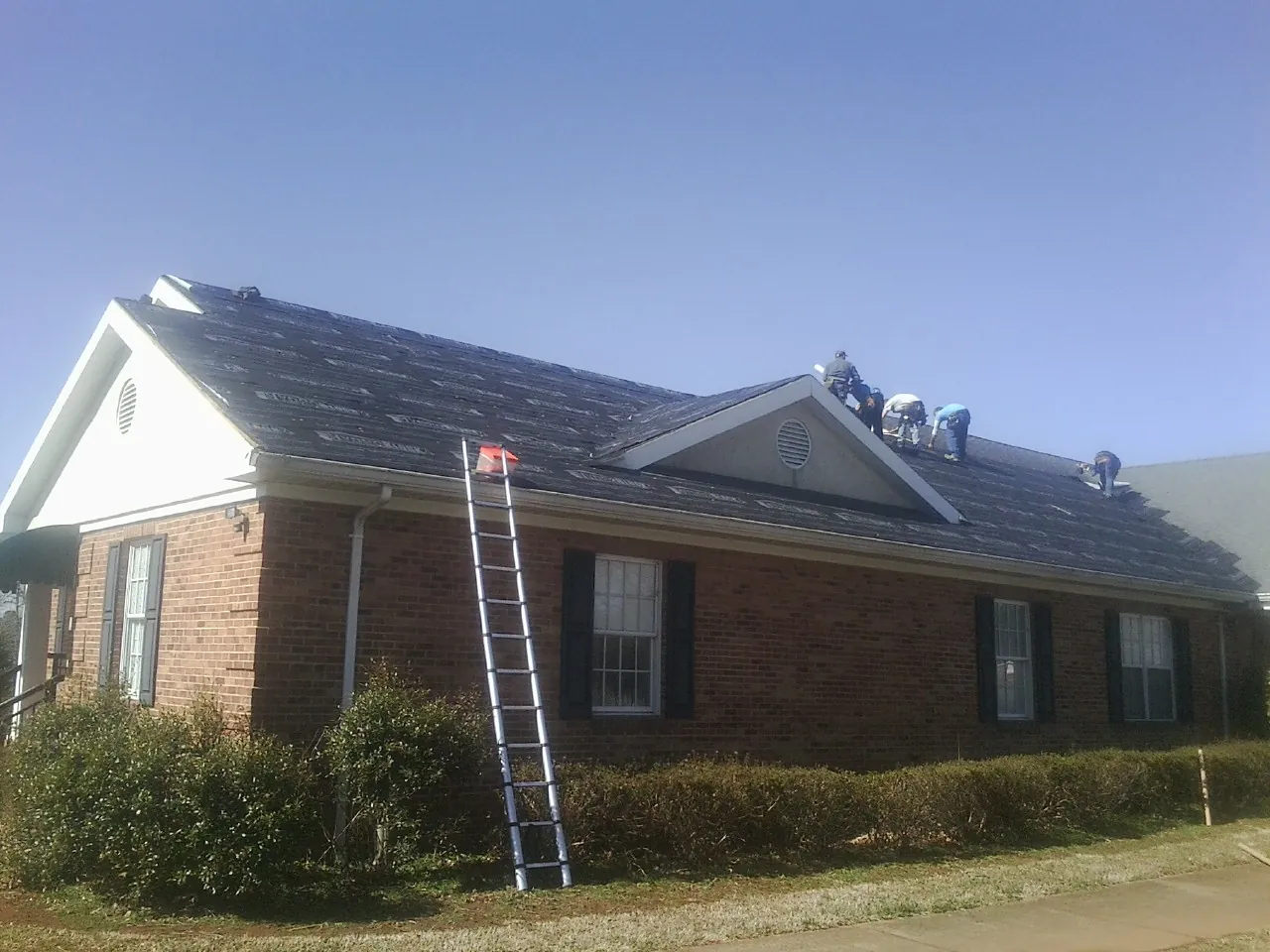 Crew tearing shingles off a brick ranch roof with a ladder set — Emergency Roof Repair work by our crew in West Lafayette