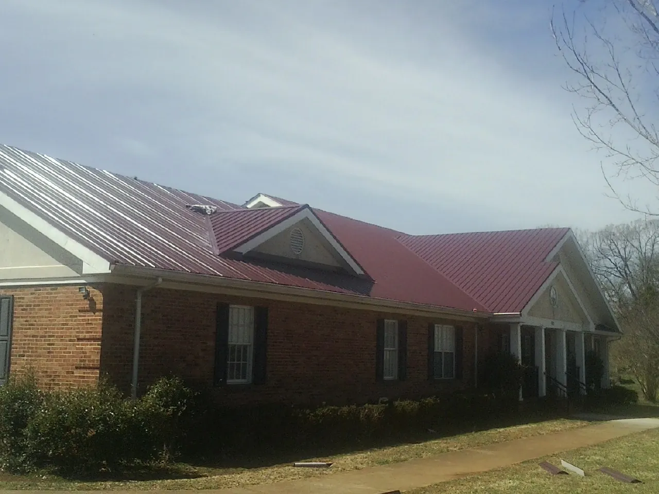 Red metal roof with gabled entries on a long brick building, from a Hail Damage Roof Repair job in West Lafayette