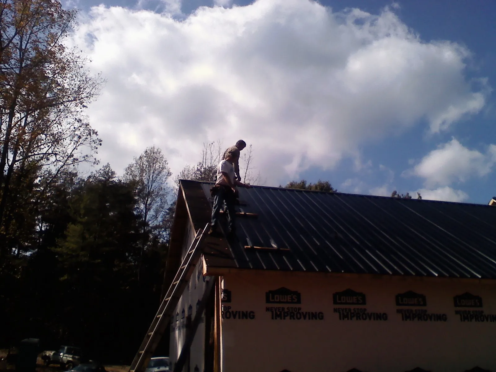 Roofer fastening dark metal panels high against a cloudy sky, from a Roof Inspection job in West Lafayette
